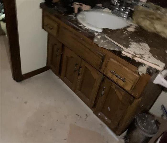 A bathroom with a vanity damaged by water and fallen drywall/insulation