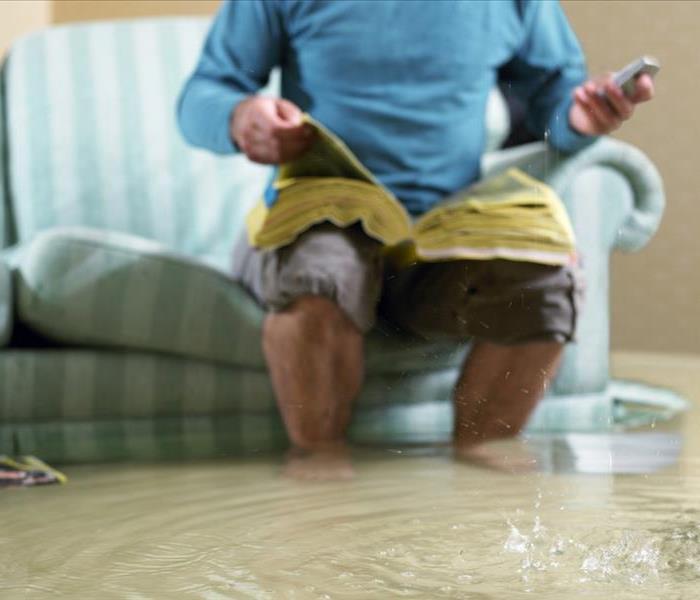 A man sitting on a couch in a flooded room, with water up to his ankles