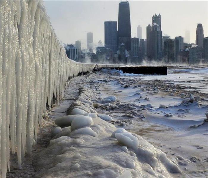 Chicago landscape in the background and the frozen lake in the foreground, with large icicles along the shoreline