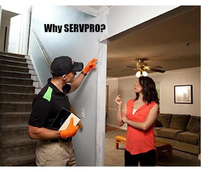 A man in a SERVPRO uniform inspecting a damaged wall with a female homeowner.