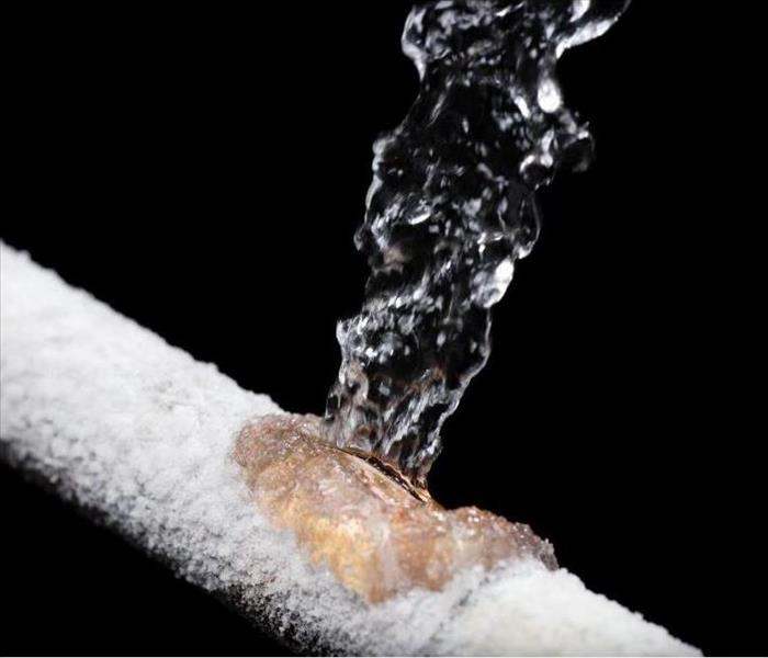 A broken metal pipe with ice forming all around it and water bursting from the crack