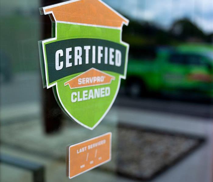 A green and orange sticker that says Certified: SERVPRO Cleaned displayed on a window