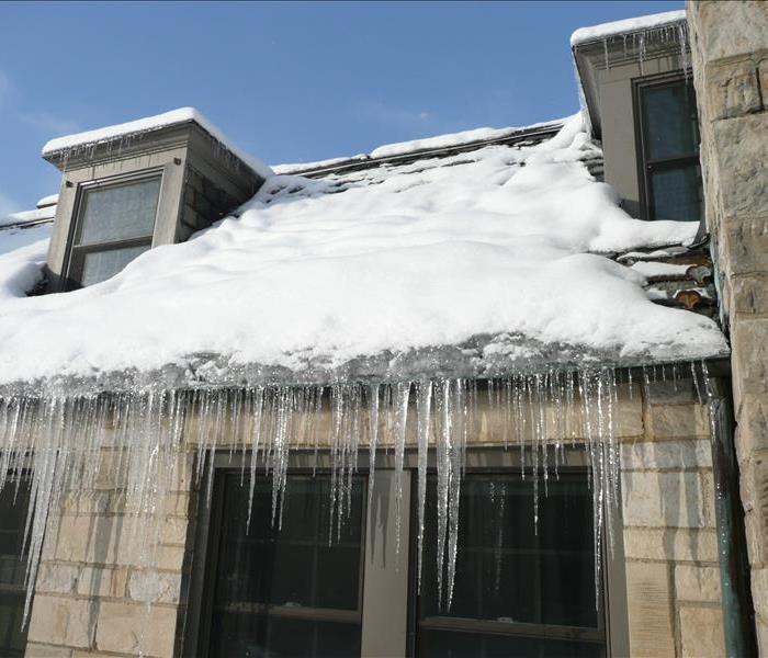 Large icicles forming from eaves of a house during daytime.